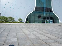 a white building with polka dots on the side of it is glassy windows and has a small green potted plant on the floor near a brick pathway