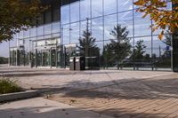 a walkway in front of an office building with some trees in the foreground, and fall foliage all around it