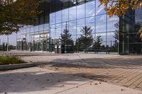 a walkway in front of an office building with some trees in the foreground, and fall foliage all around it