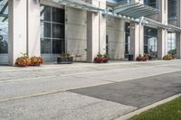 a sidewalk with flowers outside of the building with windows on it and plants in the containers next to it