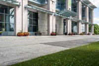 a sidewalk with flowers outside of the building with windows on it and plants in the containers next to it