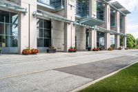 a sidewalk with flowers outside of the building with windows on it and plants in the containers next to it