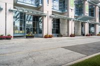 a sidewalk with flowers outside of the building with windows on it and plants in the containers next to it