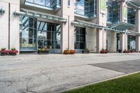 a sidewalk with flowers outside of the building with windows on it and plants in the containers next to it