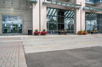 a sidewalk with flowers outside of the building with windows on it and plants in the containers next to it