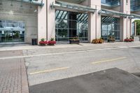 a sidewalk with flowers outside of the building with windows on it and plants in the containers next to it