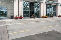 a sidewalk with flowers outside of the building with windows on it and plants in the containers next to it