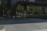 an empty bench is outside a glass building with trees reflected on the side of it