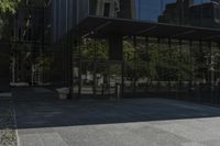 an empty bench is outside a glass building with trees reflected on the side of it