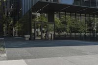 an empty bench is outside a glass building with trees reflected on the side of it