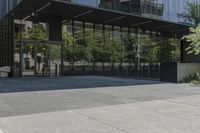 an empty bench is outside a glass building with trees reflected on the side of it