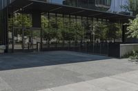 an empty bench is outside a glass building with trees reflected on the side of it