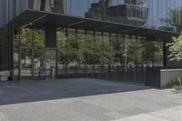 an empty bench is outside a glass building with trees reflected on the side of it