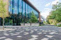 a paved walkway with tall glass windows next to trees and concrete sidewalked walkwaying