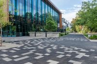 a paved walkway with tall glass windows next to trees and concrete sidewalked walkwaying