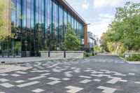 a paved walkway with tall glass windows next to trees and concrete sidewalked walkwaying