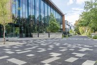 a paved walkway with tall glass windows next to trees and concrete sidewalked walkwaying