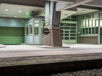 train station platform with green doors and train car on either side of train tracks and a clock on the outside of the platform