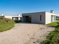 modern two story building with grass in front of it and a gravel lot in front