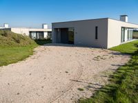 modern two story building with grass in front of it and a gravel lot in front