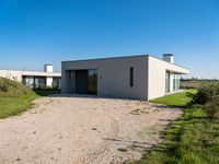 modern two story building with grass in front of it and a gravel lot in front