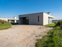 modern two story building with grass in front of it and a gravel lot in front