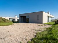 modern two story building with grass in front of it and a gravel lot in front