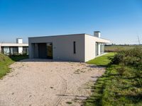 modern two story building with grass in front of it and a gravel lot in front