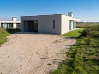 modern two story building with grass in front of it and a gravel lot in front