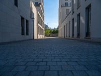 two people walking down an empty city street in an alley area with tall buildings in the background