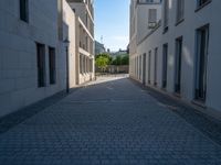 two people walking down an empty city street in an alley area with tall buildings in the background