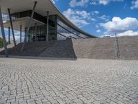 a person on a bike walking through a stone building entrance, in front of an enormous glass wall and stairs