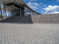 a person on a bike walking through a stone building entrance, in front of an enormous glass wall and stairs
