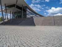 a person on a bike walking through a stone building entrance, in front of an enormous glass wall and stairs