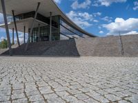 a person on a bike walking through a stone building entrance, in front of an enormous glass wall and stairs