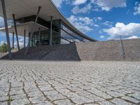 a person on a bike walking through a stone building entrance, in front of an enormous glass wall and stairs