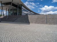 a person on a bike walking through a stone building entrance, in front of an enormous glass wall and stairs