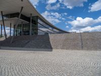 a person on a bike walking through a stone building entrance, in front of an enormous glass wall and stairs