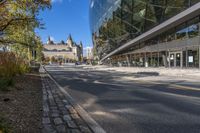 street in city with large tall glass building along the side of the sidewalk and trees along the walkway