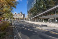 street in city with large tall glass building along the side of the sidewalk and trees along the walkway