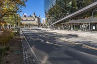 street in city with large tall glass building along the side of the sidewalk and trees along the walkway