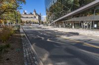 street in city with large tall glass building along the side of the sidewalk and trees along the walkway