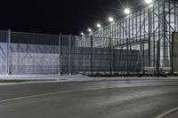 the tall gate is behind an empty parking lot at night time at the edge of a street