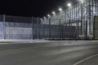 the tall gate is behind an empty parking lot at night time at the edge of a street