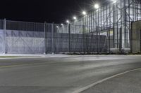 the tall gate is behind an empty parking lot at night time at the edge of a street