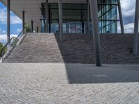 a person on a bike walking through a stone building entrance, in front of an enormous glass wall and stairs