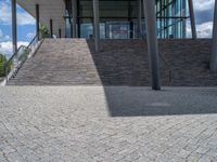 a person on a bike walking through a stone building entrance, in front of an enormous glass wall and stairs