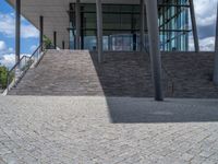 a person on a bike walking through a stone building entrance, in front of an enormous glass wall and stairs