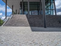 a person on a bike walking through a stone building entrance, in front of an enormous glass wall and stairs