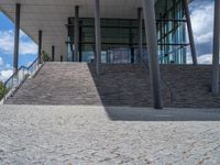 a person on a bike walking through a stone building entrance, in front of an enormous glass wall and stairs